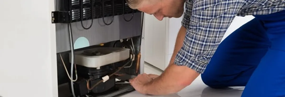 Refrigerator repair technician servicing the compressor and condenser area in New Haven, CT