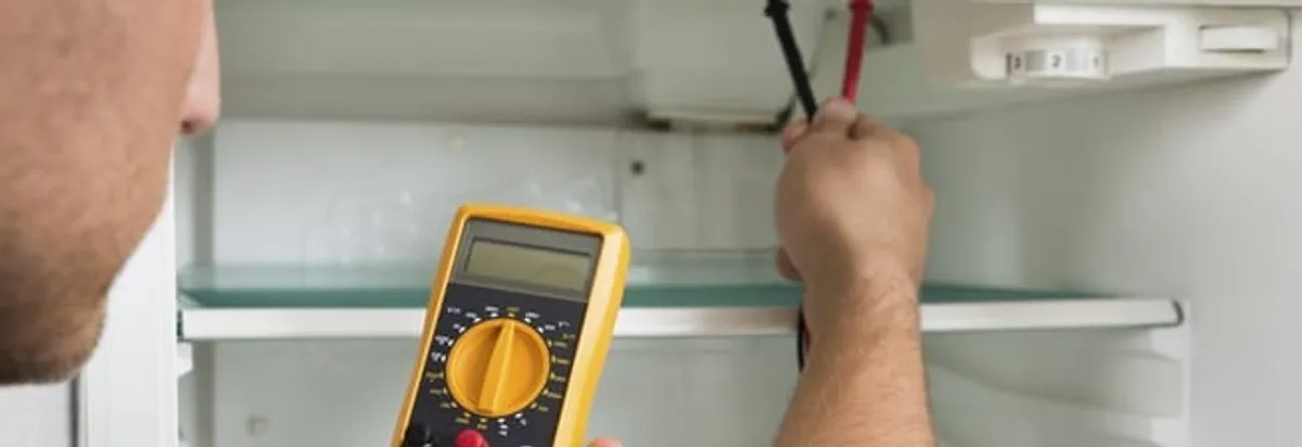 Refrigerator repair technician testing electrical components with a multimeter in New Haven, CT